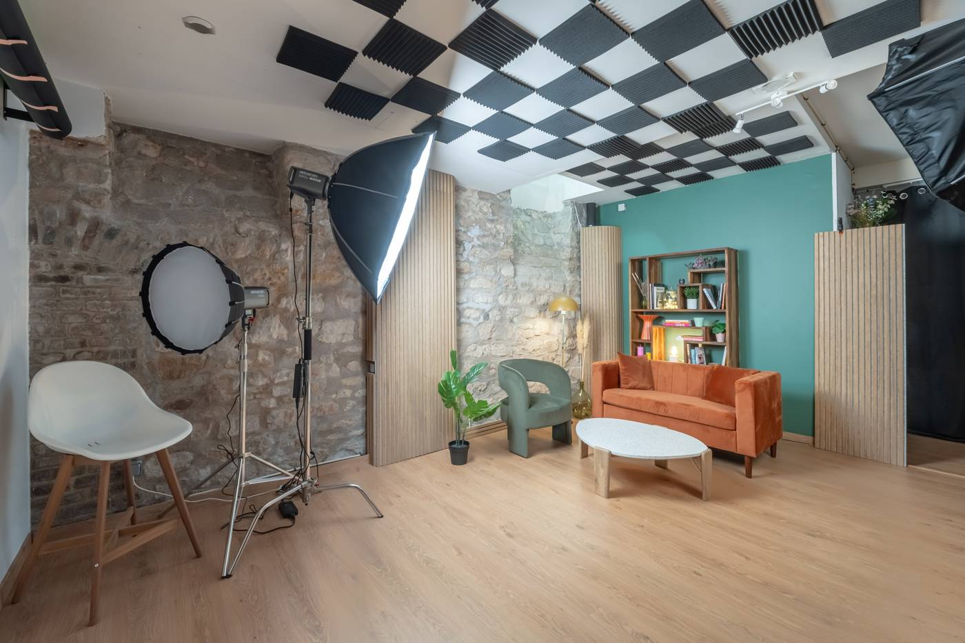 Espace cosy : canapé orange, fauteuil vert, mur en pierre et bibliothèque